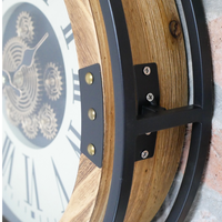 industrial wall clock with exposed moving gears, black metal frame, wood accents, and Roman numeral dial mounted on a dark paneled wall.