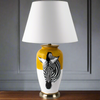 A ceramic table lamp with a yellow and white base featuring a black zebra stripe design, completed with a white fabric shade on top.