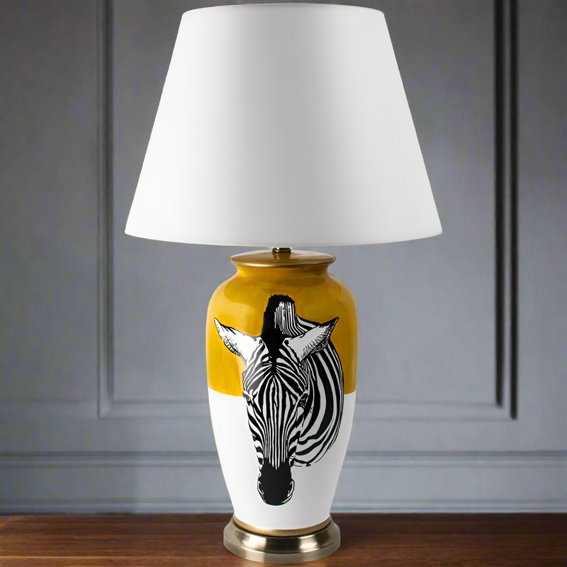 A ceramic table lamp with a yellow and white base featuring a black zebra stripe design, completed with a white fabric shade on top.
