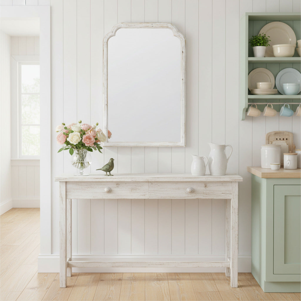 Tall, distressed white wooden mirror with shaping to the frame over a distressed console in a Scandi style kitchen.